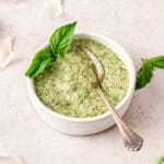 creamy basil pesto in small bowl with spoon and fresh basil