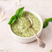 creamy basil pesto in small bowl with spoon and fresh basil