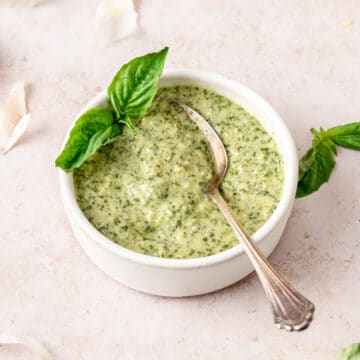 creamy basil pesto in small bowl with spoon and fresh basil