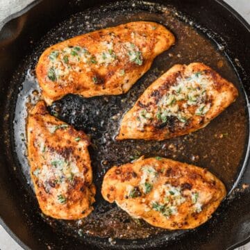 close up of cast iron chicken breasts with garlic butter.