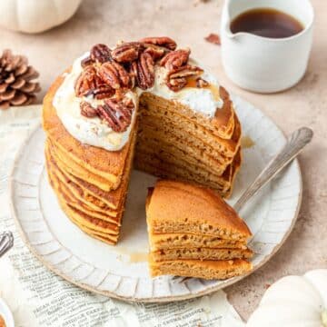 stack of sourdough pumpkin pancakes topped with whipped cream and toasted pecans.