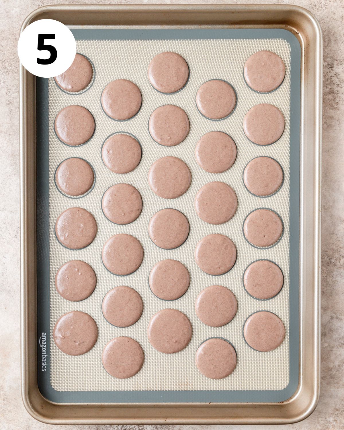 chocolate macarons piped on baking sheet.