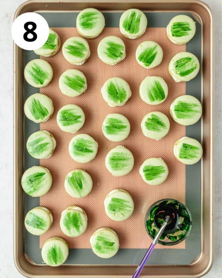 painting tops of macarons with green food coloring.